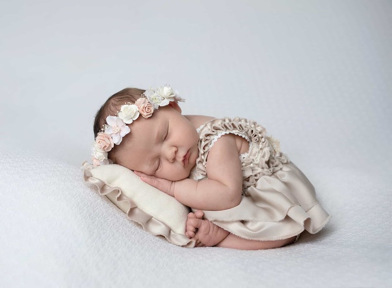 A newborn girl posed on a pillow wearing a flower crown during a newborn portrait session at Bobi Biederman Photography studio.