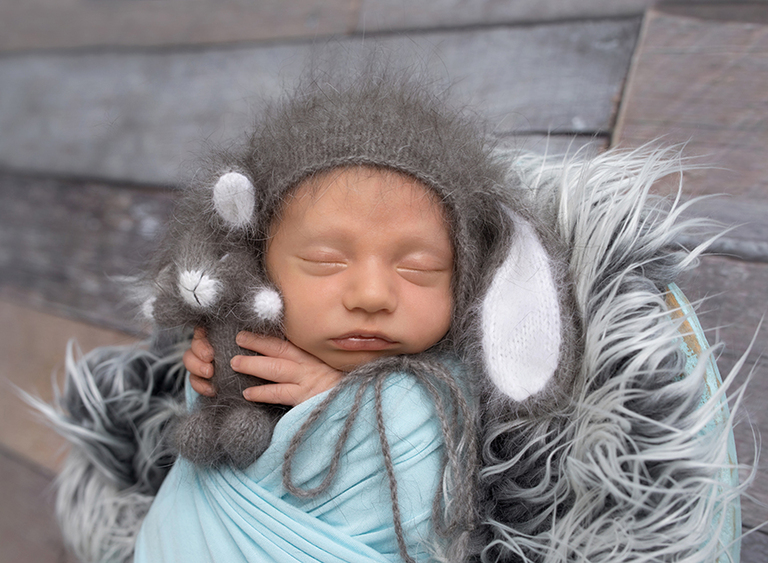 Portrait of newborn boy in a bowl with a bunny hat and stuffie