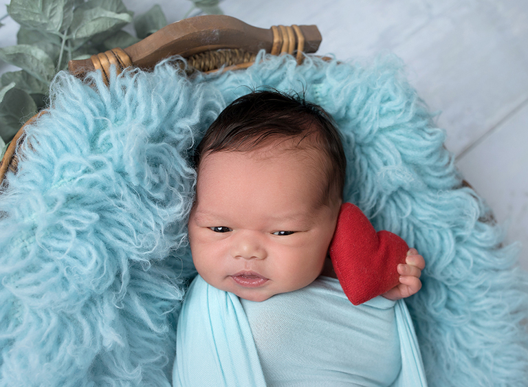 Newborn baby boy with adorable hair in blue with a heart
